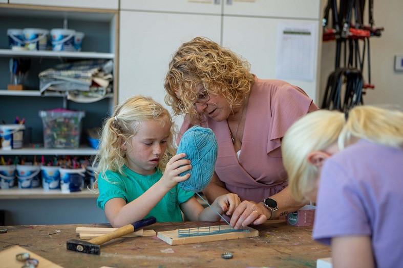 kind maakt knutselwerk met hout, wol en spijkers