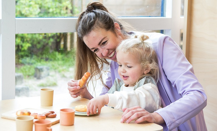 Pedagogisch medewerker met kindje aan tafel