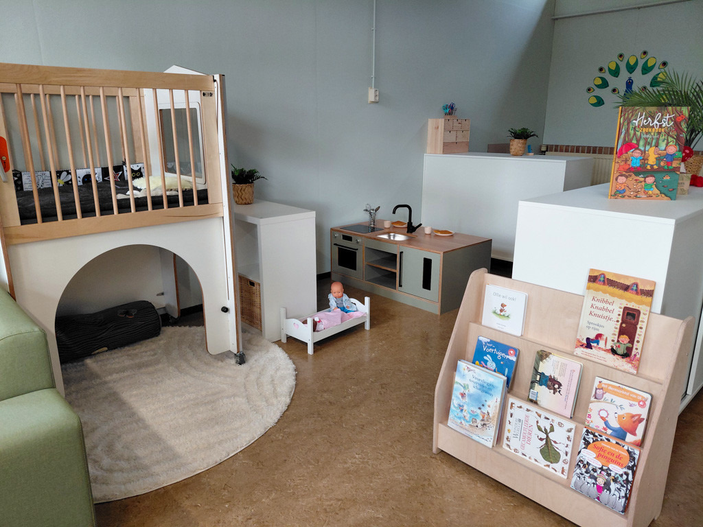 De speelhoek van kinderdagverblijf de Bangert in Andijk. In de speelhoek staat een houten speelmeubel met slaapruimte, kinderkeuken, poppenbedje en een boekenrek met prentenboeken.