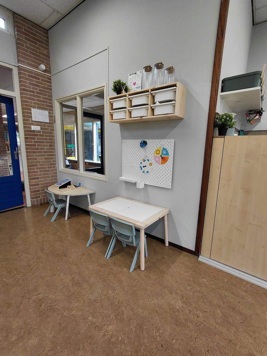 Creatieve werkhoek in kinderdagverblijf en peuterspeelgroep De Bangert in Andijk met twee kinderwerktafels, stoelen, opbergvakken en pegboard voor activiteiten.