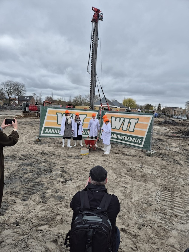 Symbolische eerste paal bij de bouw van Kindcentrum Spanbroek, met betrokkenen in bouwkleding en oranje helmen