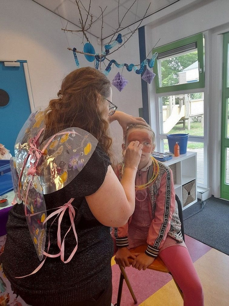 meisje wordt geschminkt door pedagogisch professional met vlinder vleugels om