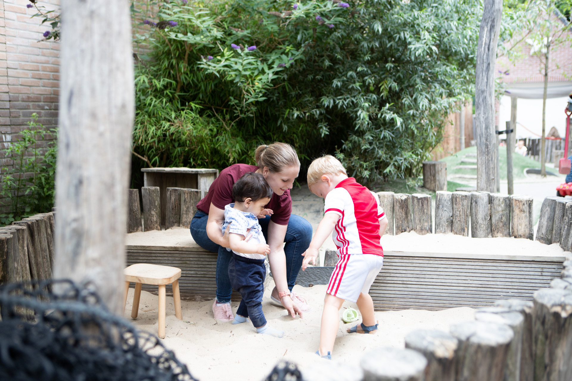 pedagogisch professional met twee kinderen buiten in de zandbak