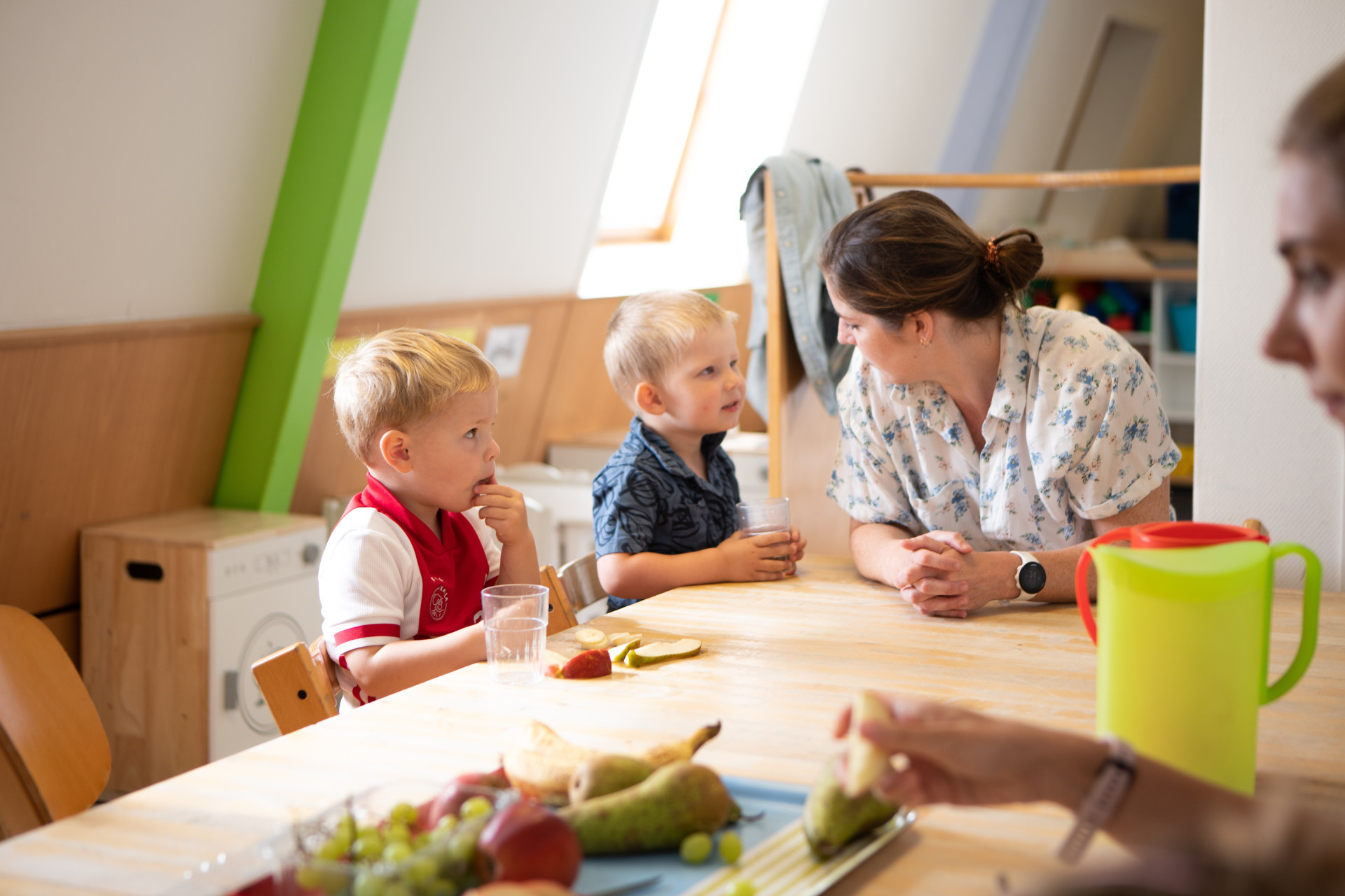 Kinderen eten fruit aan tafel samen met pedagogisch medewerker