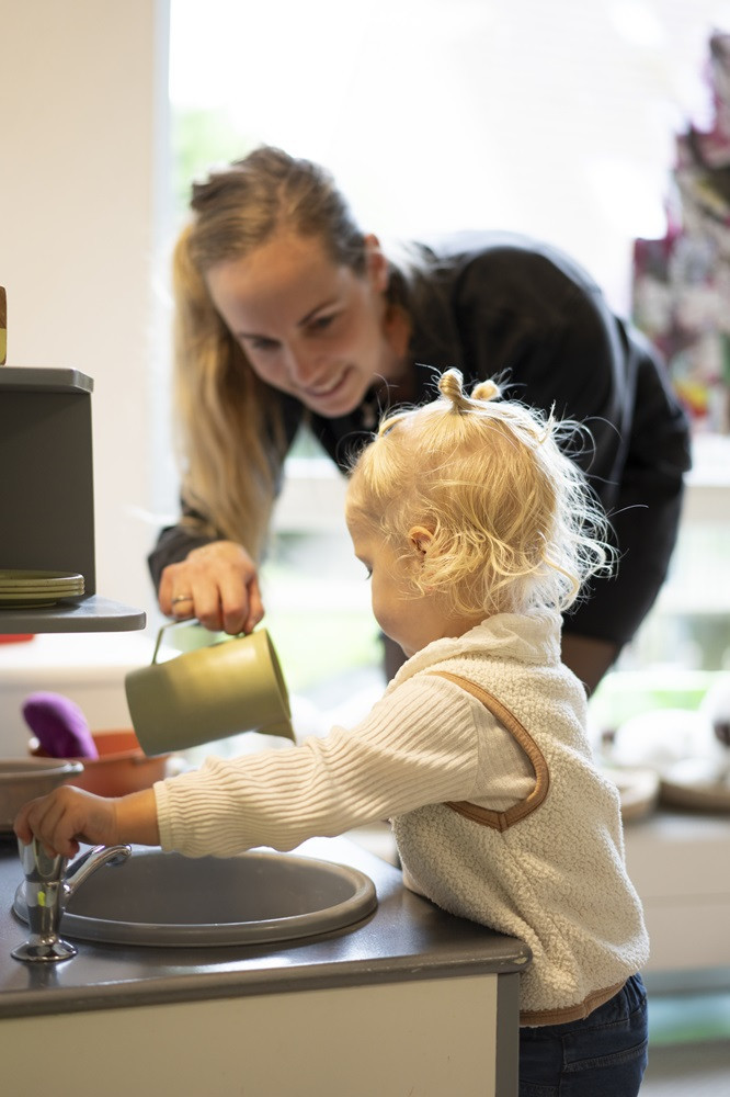 kind speelt samen met pedagogisch professional in speelkeuken