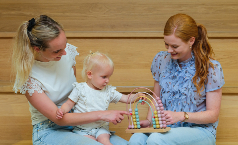Pedagogisch professionals spelen samen met een peuter met een houten telraam bij Kinderopvang Berend Botje