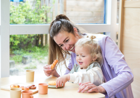 Pedagogisch medewerker en kind spelen aan tafel