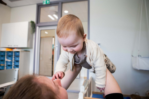 Pedagogisch medewerker houdt baby in de lucht