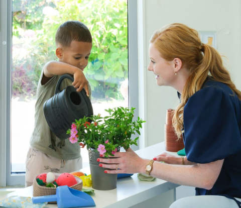 pedagogisch professional helpt jongen met plant water geven