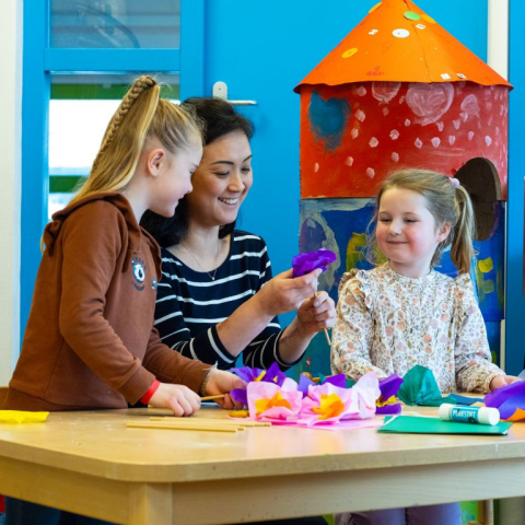 pedagogisch medewerker en twee kinderen maken papieren bloemen
