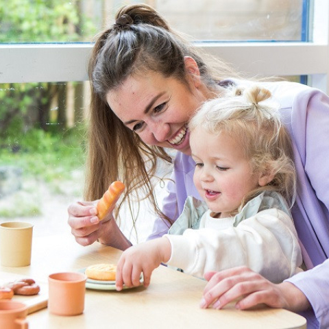 Pedagogisch medewerker met kindje aan tafel