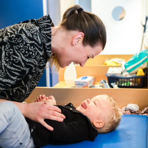 pedagogisch medewerker en peuter lachen naar elkaar
