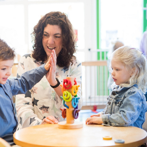 Pedagogisch medewerker geeft high five aan peuter