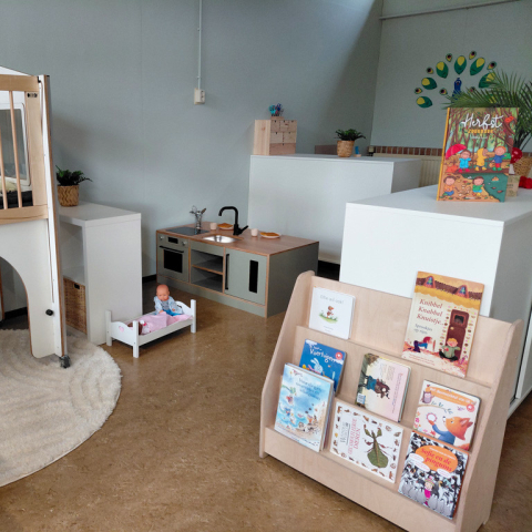 De speelhoek van kinderdagverblijf de Bangert in Andijk. In de speelhoek staat een houten speelmeubel met slaapruimte, kinderkeuken, poppenbedje en een boekenrek met prentenboeken.